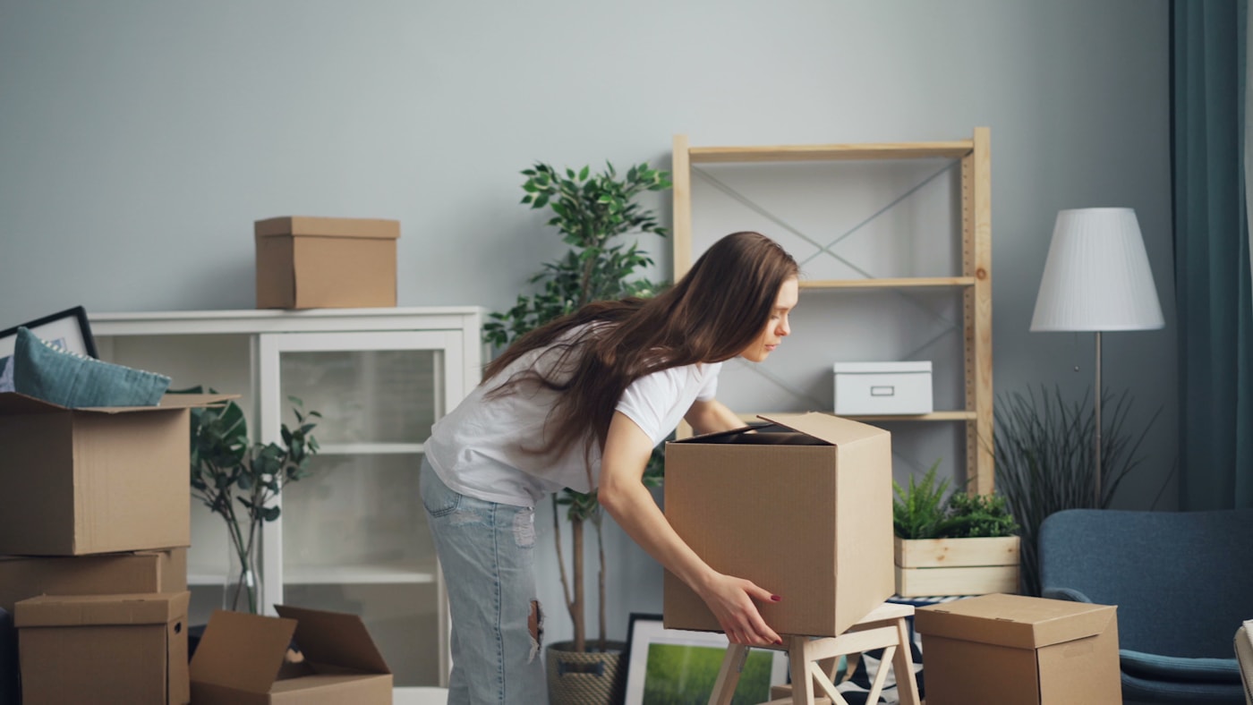 Woman carrying a packed cardboard box through a room prepared for moving day
