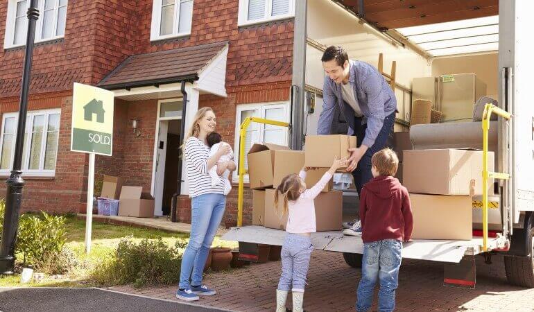 Family unloading moving boxes from a removal lorry outside a UK brick house